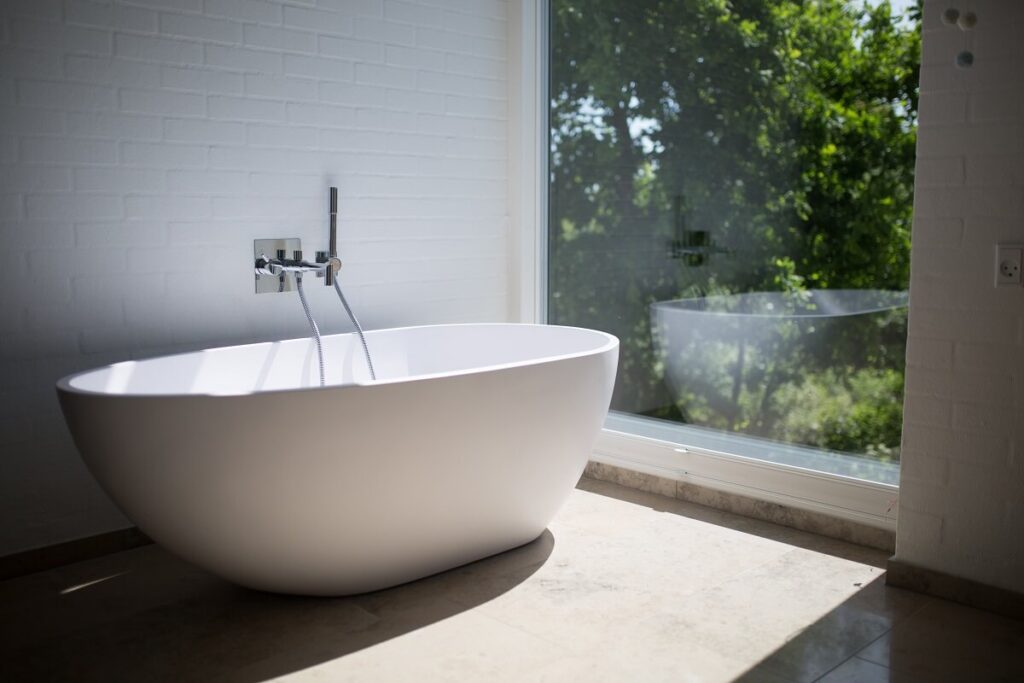 Free standing acrylic bathtub in front of picture window in renovated bathroom