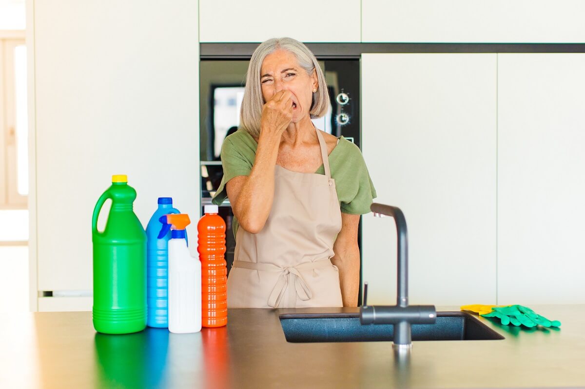 Woman at the kitchen sink holding her nose due to smelly drains