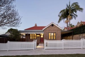 Simple family home in Chatswood in North Sydney with red roof and white picket fence. Palm trees in background. Serviceable area for Gladesville Plumbing Services.
