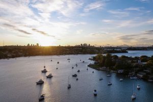 Paramatta River with lots of boats by Gladesville shoreline. City skyline in the back with sun setting behind. Home of Gladesville Plumbing Services.