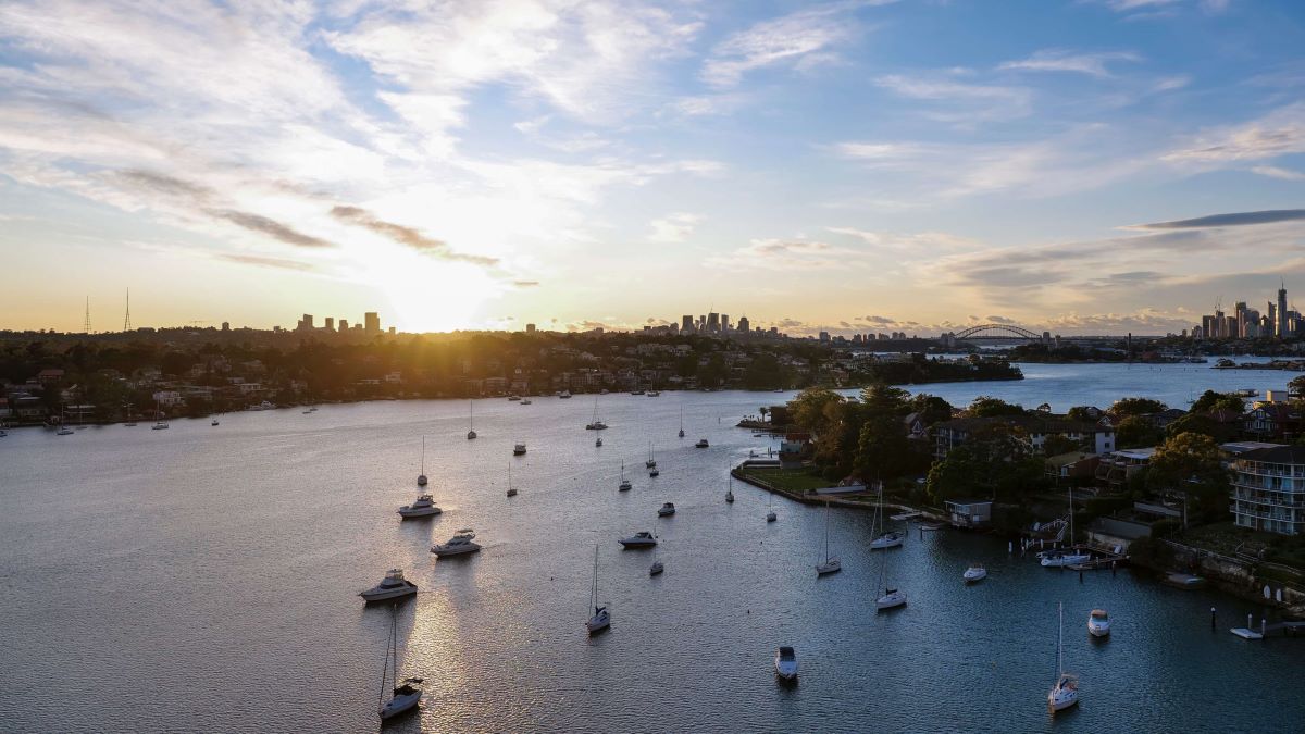 Paramatta River with lots of boats by Gladesville shoreline. City skyline in the back with sun setting behind. Home of Gladesville Plumbing Services.