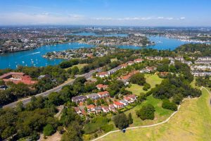View from the sky of Huntleys Cove. Few rows of large homes with red rooves in between lots of deep green and large trees. Streets in waving fashion seemingly mimicking Paramatta River. Houses closer together further towards the river. Gladesville Plumbing Services service area.