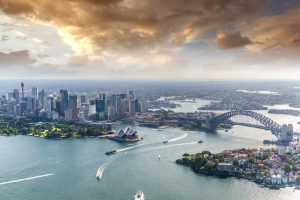 Wide view of bustling Sydney CBD, Story Bridge and Paramatta River. Cloudy sky and high rises on the left and suburbs on the right. Gladesville Plumbing Services also services Sydney CBD.