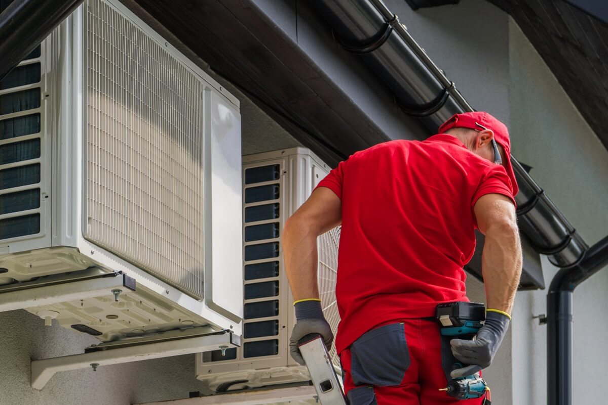 Professional plumber fixing gutter leak on ladder reaching for drill on his back pocket. Roofline gutters above him and home in North Sydney.