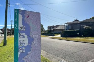 Street in Melrose Park featuring sign of riverwalk map. Simple suburban house in background. Gladesville Plumbing Services emergency service area.