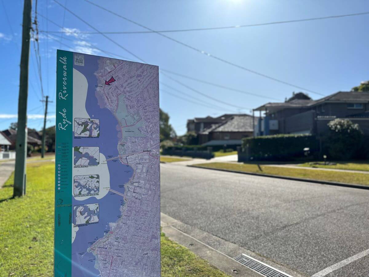 Street in Melrose Park featuring sign of riverwalk map. Simple suburban house in background. Gladesville Plumbing Services emergency service area.