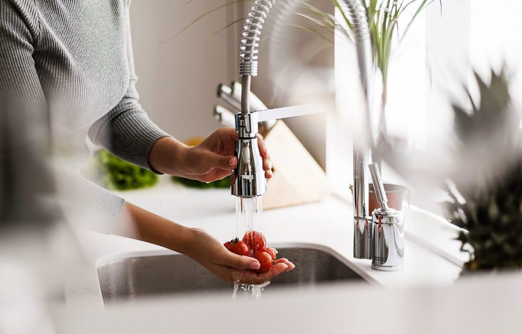 Woman using kitchen pull out spray mixer or flexitap to rinse vegetables