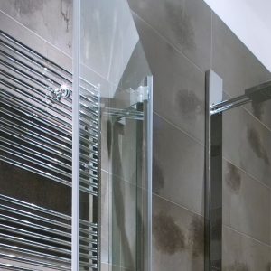 Chrome plated hydronic heated towel rail installed in bathroom.
