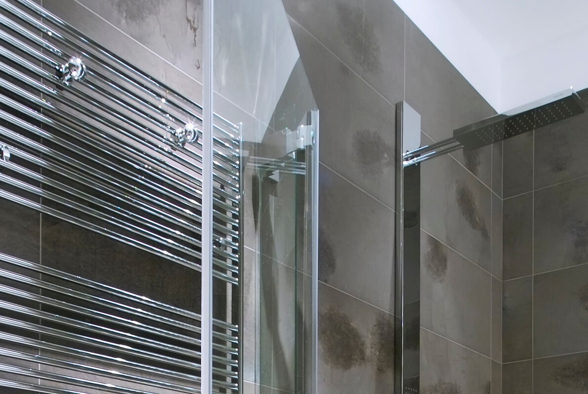 Chrome plated hydronic heated towel rail installed in bathroom.
