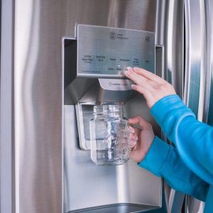 Woman at shiny fridge filling up mason jar with water. Properly plumbed fridge with sparkling water and pure water filter installation. Plumbing services available for North Sydney.