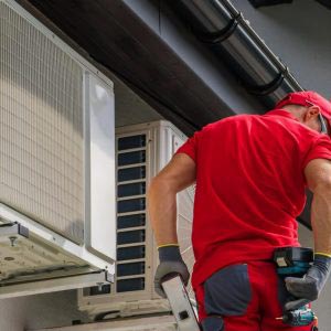 Professional plumber fixing gutter leak on ladder reaching for drill on his back pocket. Roofline gutters above him and home in North Sydney.