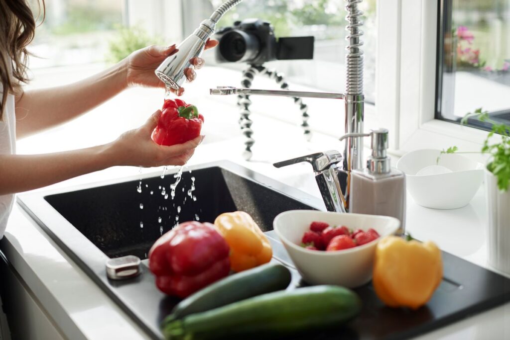 Kitchen tapware - woman using flexi hose tapware in the kitchen to rinse vegetables