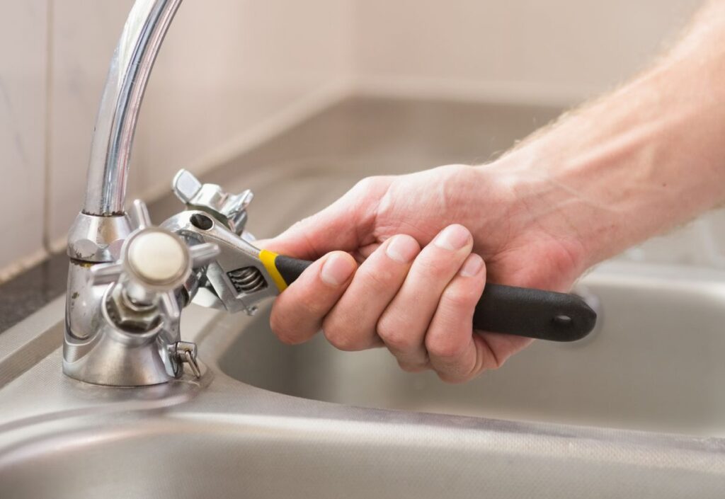 DIY plumbing being performed by man changing washers on kitchen sink tap.